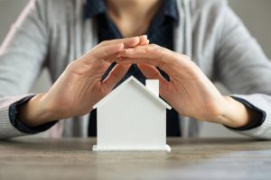 Hands sheltering a small white house model, symbolising apartment insurance protection in Dubai